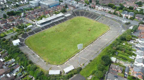 PA Media An aerial view of a grass pitch with concrete terrace-style stands. It sits in a residential area with a number of red brick houses surrounding the site.